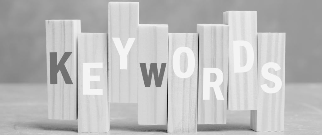 Wooden blocks spell out KEYWORDS in bold, alternating tones, against a grey background—a visual guide to keywords in SEO.
