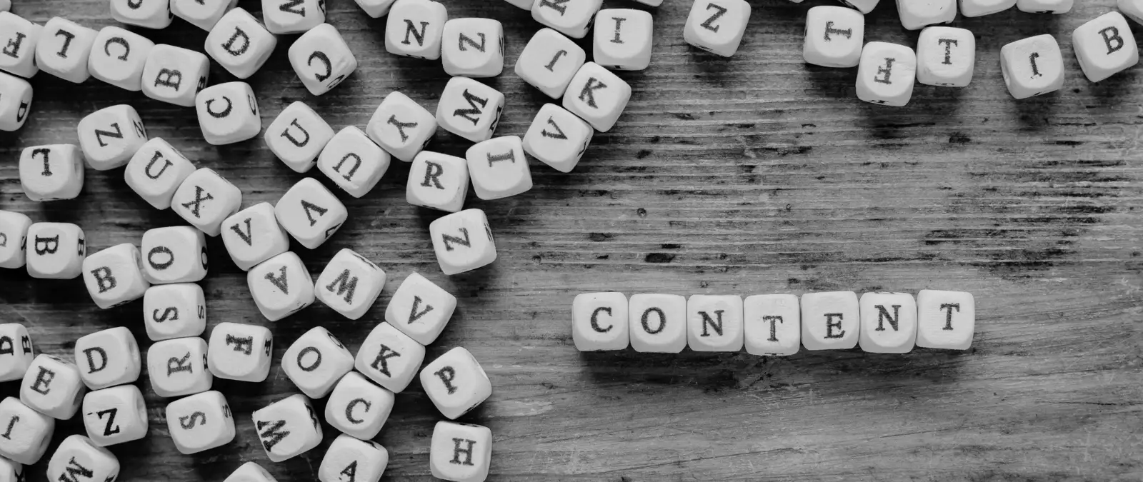 Scattered letter blocks on a wooden surface, with some blocks neatly arranged to spell the word CONTENT in the centre-right. The image, presented in black and white, subtly evokes themes of on-page SEO optimisation through its focus on the importance of well-organised content.